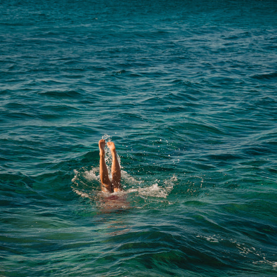 Legs of a person diving into the sea with their torso under the water’s surface.