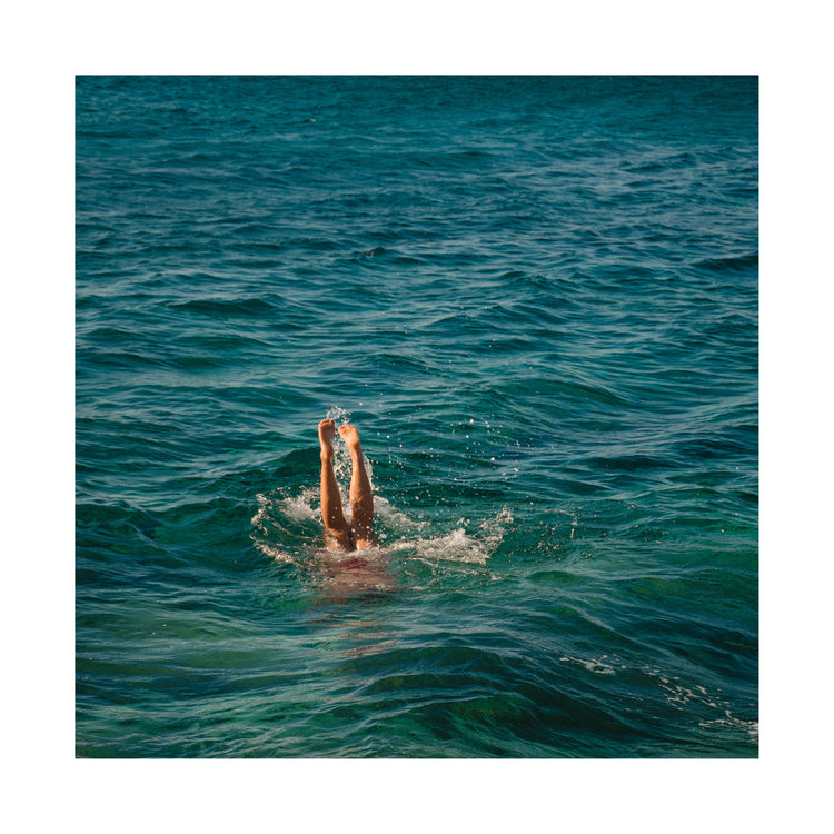 Legs of a person diving into the sea with their torso under the water’s surface.