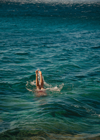 Legs of a person diving into the sea with their torso under the water’s surface.