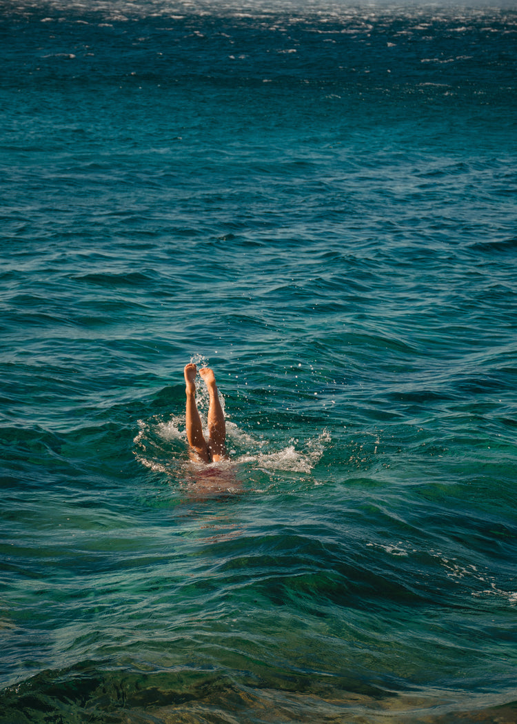 Legs of a person diving into the sea with their torso under the water’s surface.