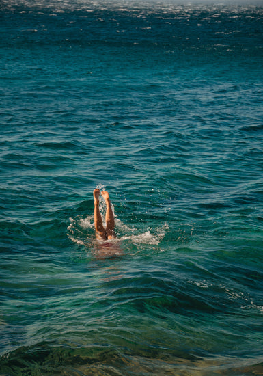 Legs of a person diving into the sea with their torso under the water’s surface.