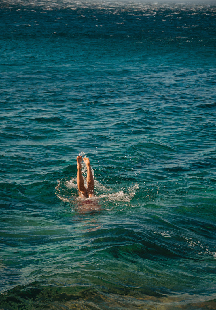 Legs of a person diving into the sea with their torso under the water’s surface.