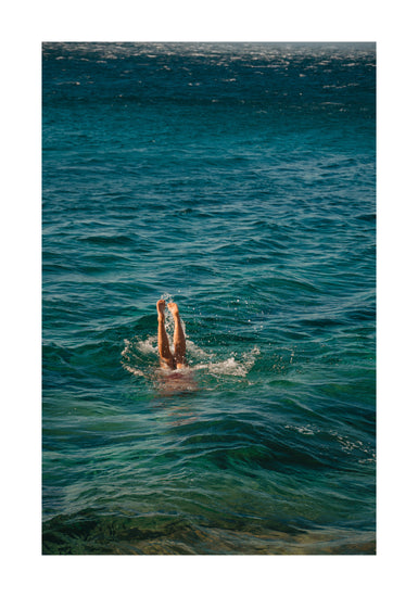 A person dives into the ocean during a morning swim, their legs just above the water. The sea reveals deep and light blue hues, with waves embracing them—a scene captured in the Morning Dip Poster reminiscent of a Lavinia Cernau wall-hanging.