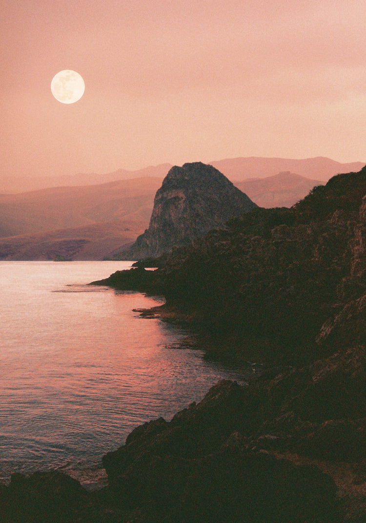 Full moon shining bright over the coastline set in a mountain scenery.