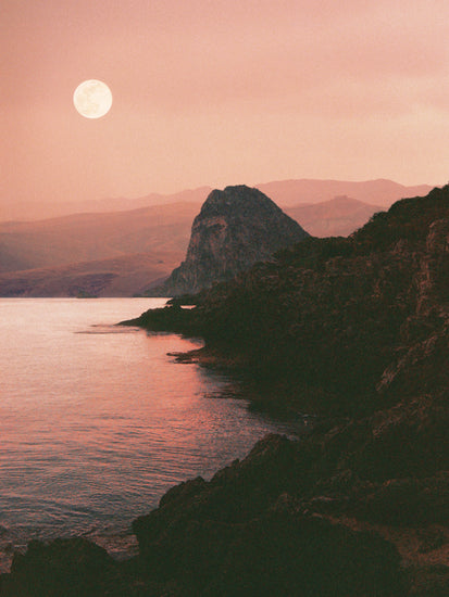 Full moon shining bright over the coastline set in a mountain scenery.