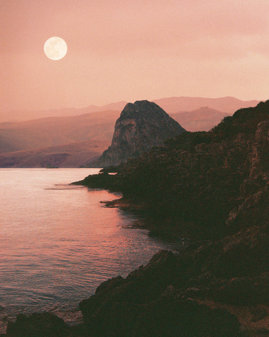Full moon shining bright over the coastline set in a mountain scenery.
