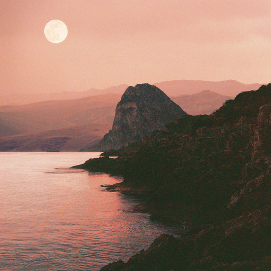 Full moon shining bright over the coastline set in a mountain scenery.