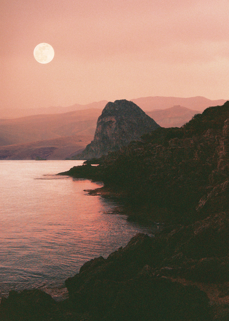 Full moon shining bright over the coastline set in a mountain scenery.