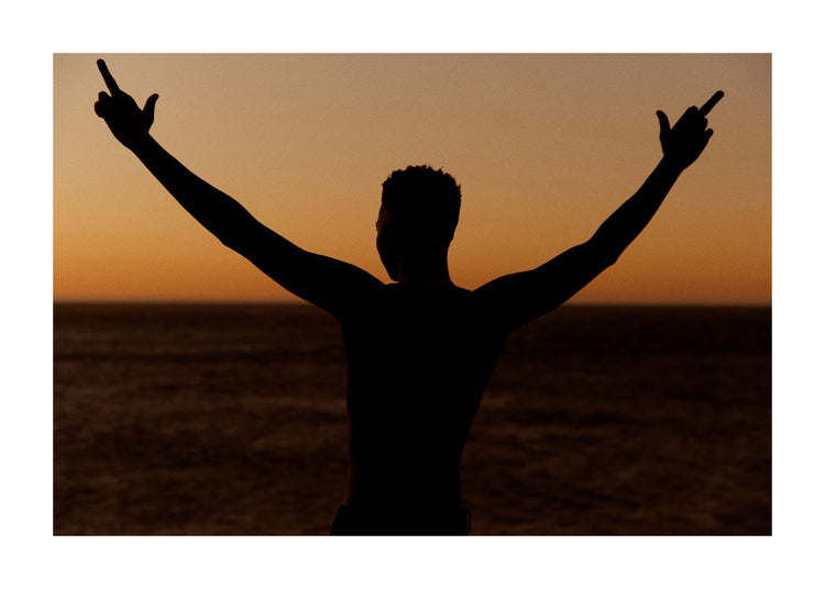 Man standing in front of a sea at sunset and flipping everybody off.