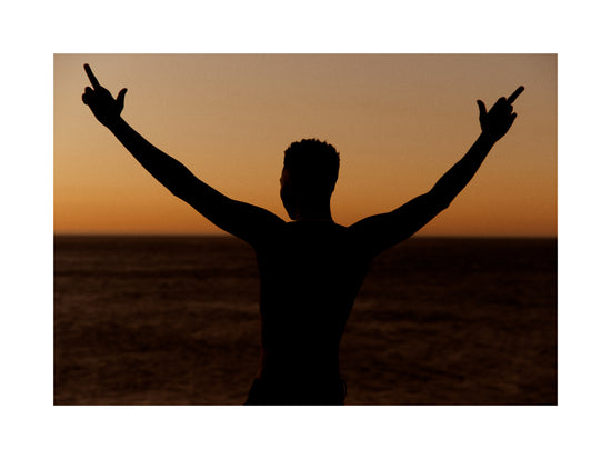 Man standing in front of a sea at sunset and flipping everybody off.