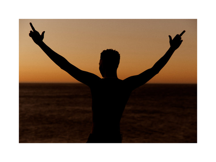 Man standing in front of a sea at sunset and flipping everybody off.