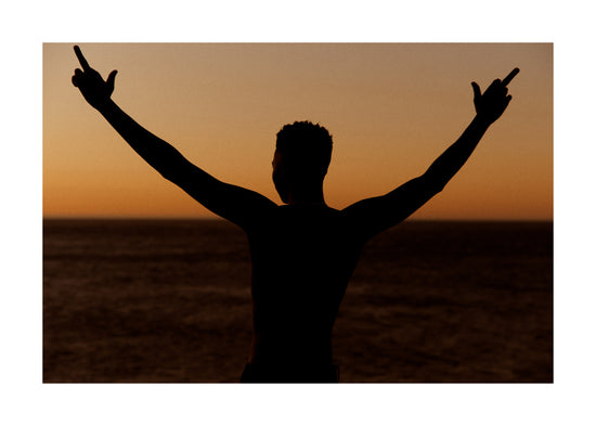 Man standing in front of a sea at sunset and flipping everybody off.