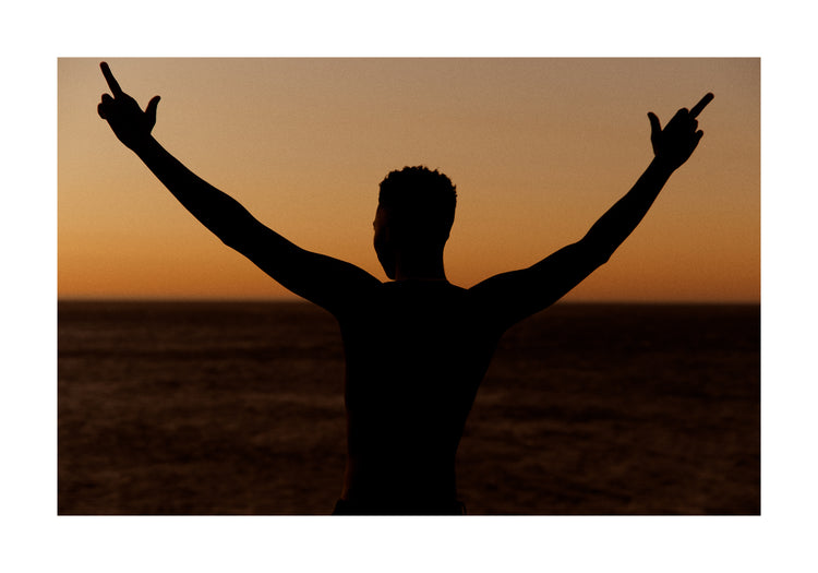 Man standing in front of a sea at sunset and flipping everybody off.