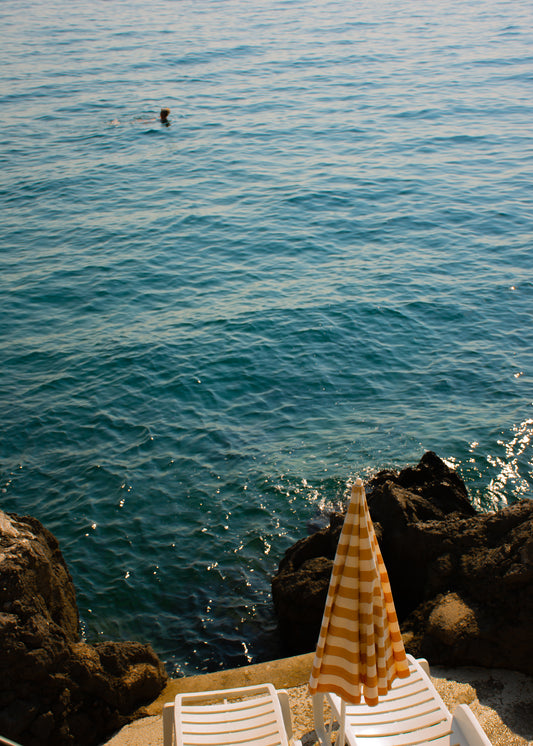 Tanning beds and a beach umbrella on the shore of the blue, Croatian sea.