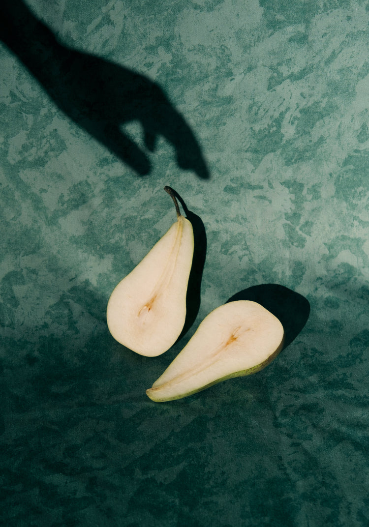 Still life of a pear cut in half and a shadow of a hand reaching for it.
