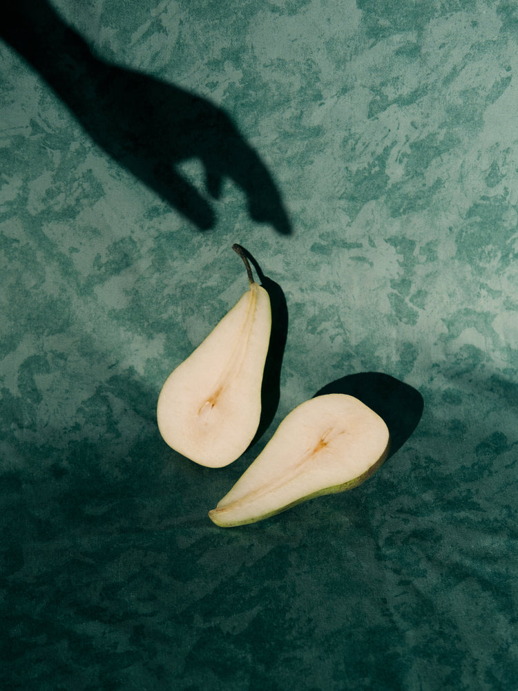 Still life of a pear cut in half and a shadow of a hand reaching for it.