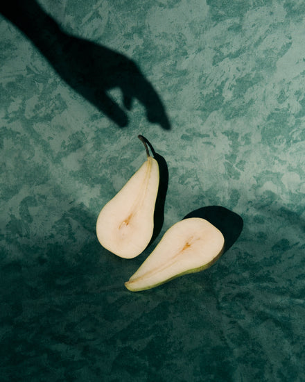 Still life of a pear cut in half and a shadow of a hand reaching for it.