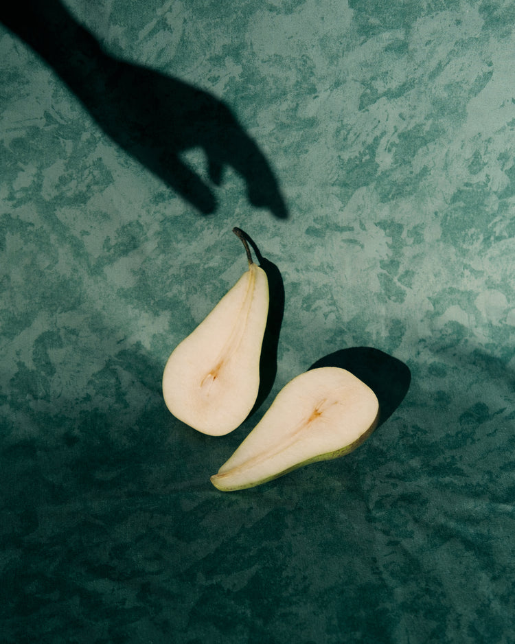 Still life of a pear cut in half and a shadow of a hand reaching for it.