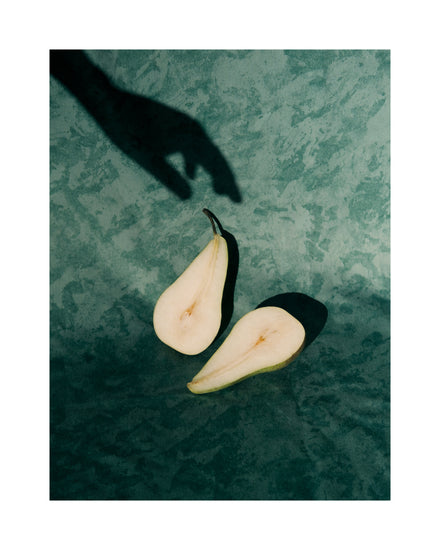 Still life of a pear cut in half and a shadow of a hand reaching for it.