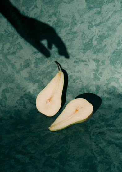 Still life of a pear cut in half and a shadow of a hand reaching for it.