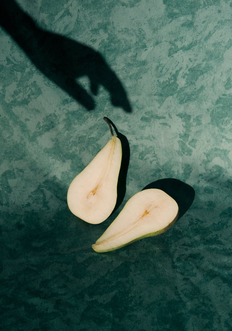 Still life of a pear cut in half and a shadow of a hand reaching for it.