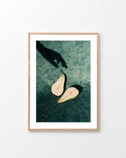 Still life of a pear cut in half and a shadow of a hand reaching for it.