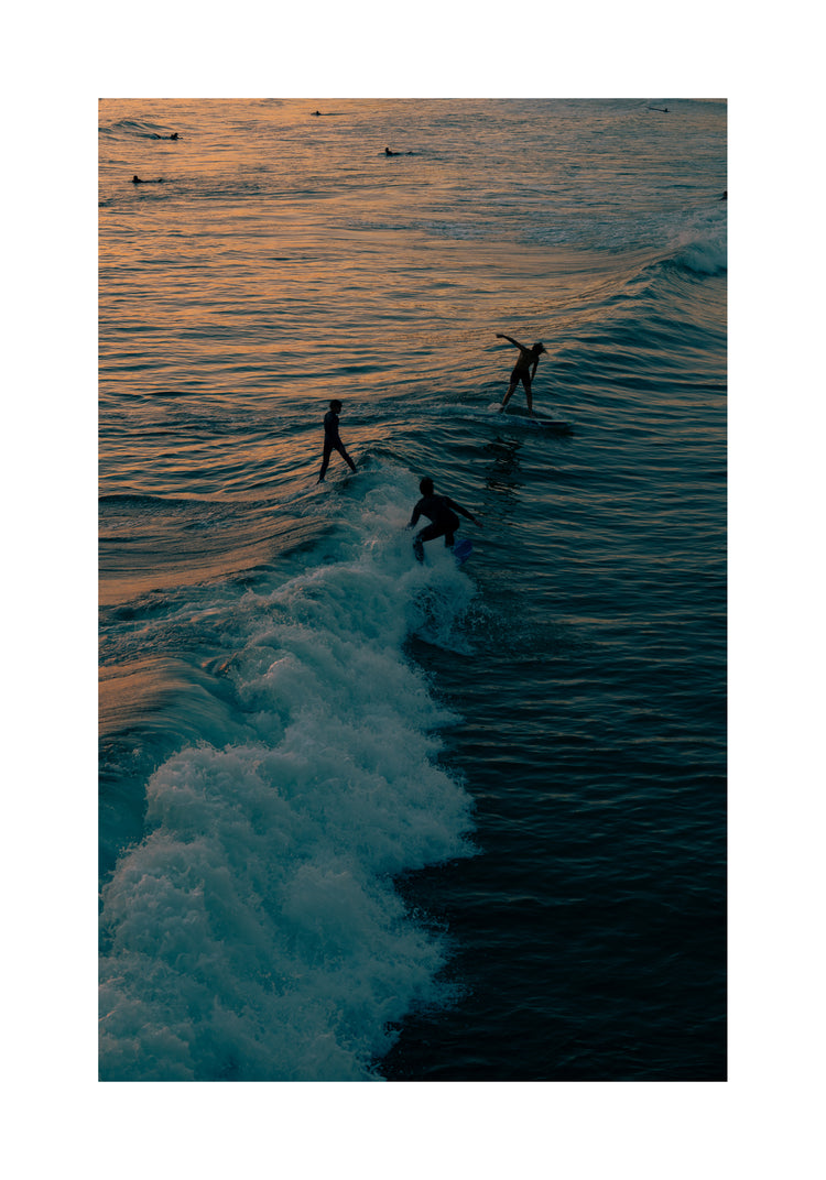 Surfers playing in the last waves of the day as the sun goes down.