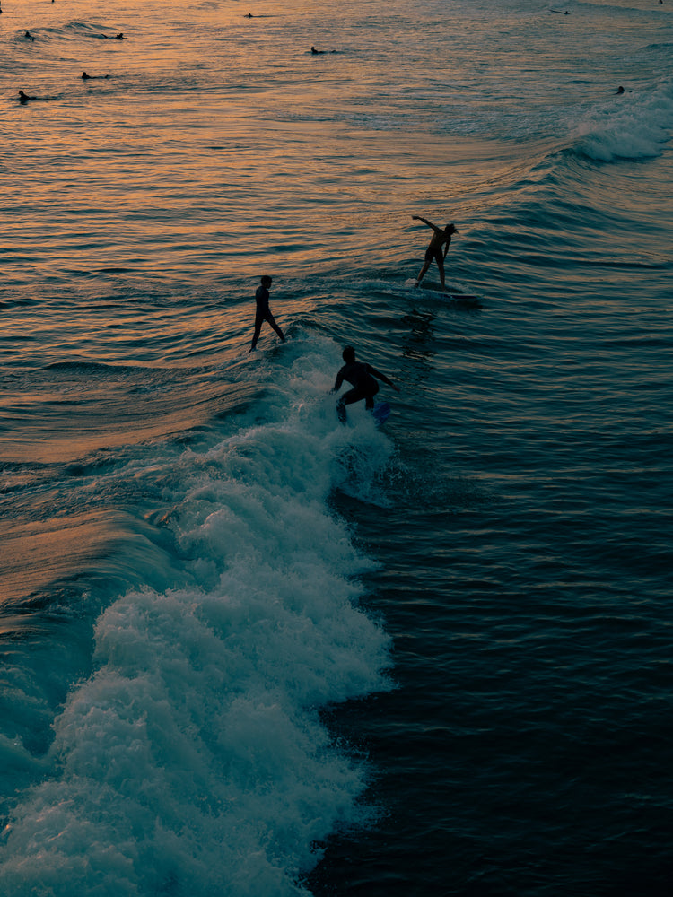 Surfers playing in the last waves of the day as the sun goes down.