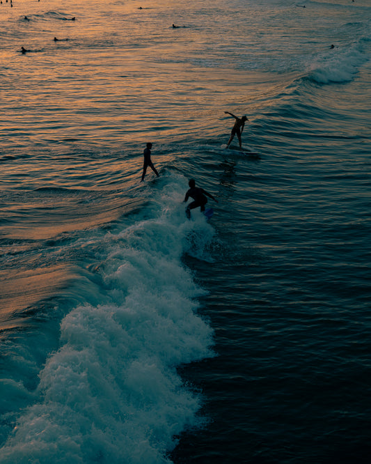 Surfers playing in the last waves of the day as the sun goes down.
