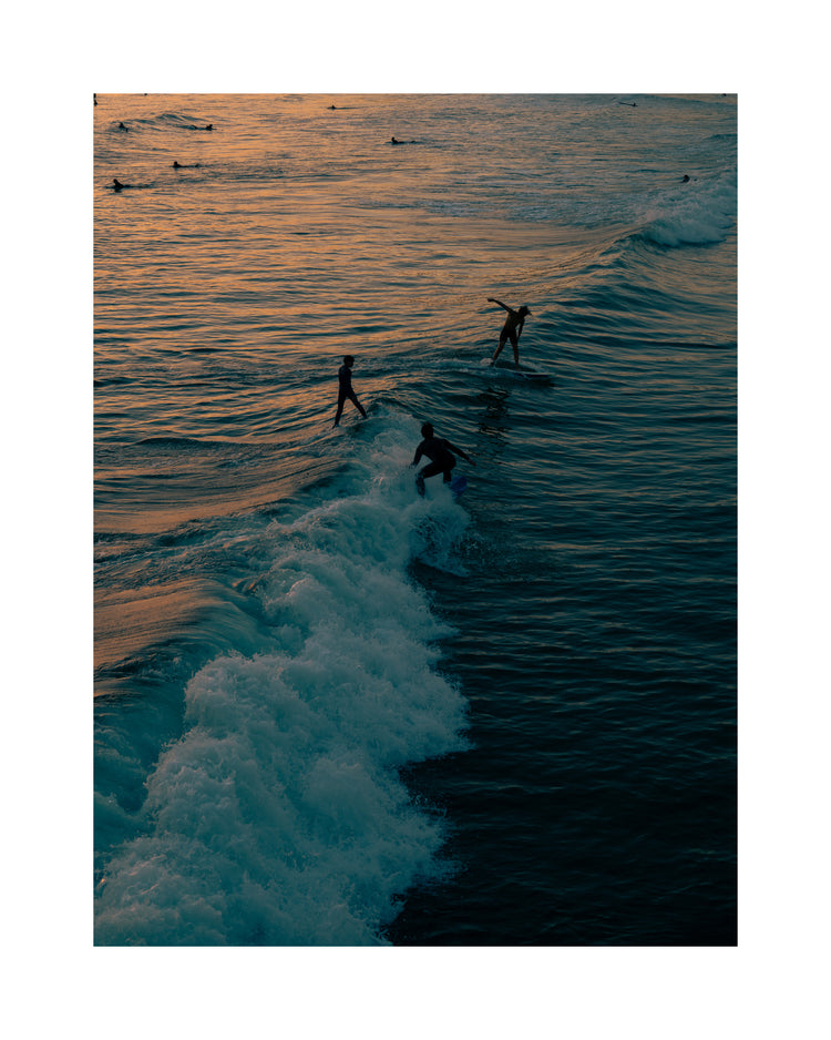Surfers playing in the last waves of the day as the sun goes down.