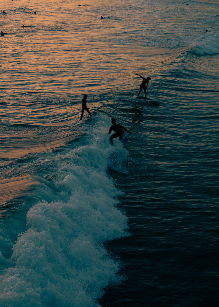 Surfers playing in the last waves of the day as the sun goes down.