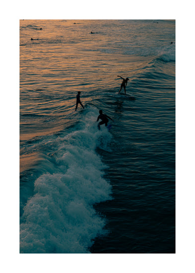 Surfers playing in the last waves of the day as the sun goes down.