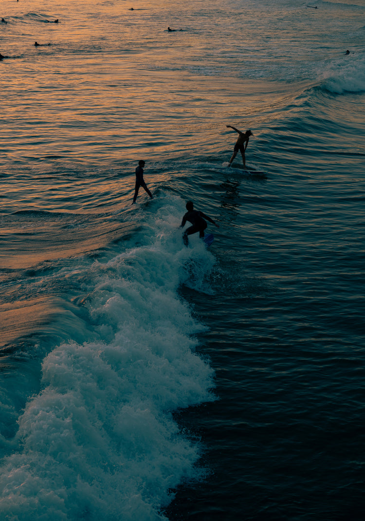Surfers playing in the last waves of the day as the sun goes down.