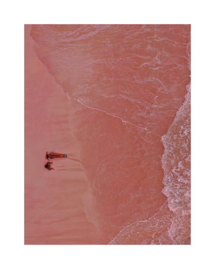 Pink beach with a woman and a child sitting on the shore.