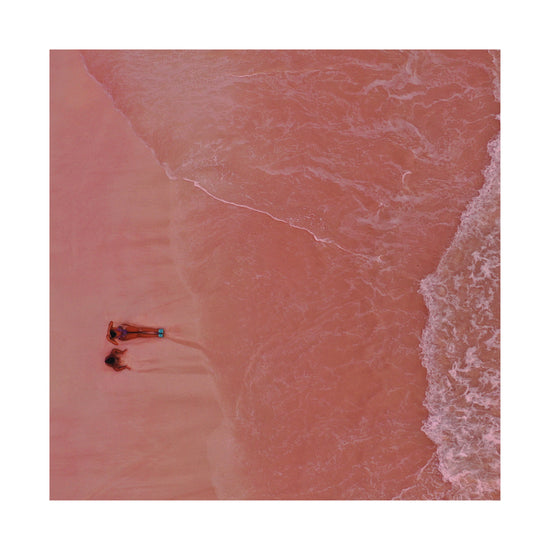 Pink beach with a woman and a child sitting on the shore.