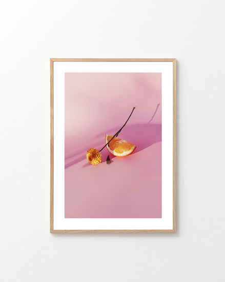 Still life portrait of an orange and a flower on a pink surface.