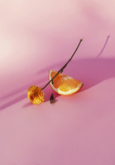 Still life portrait of an orange and a flower on a pink surface.