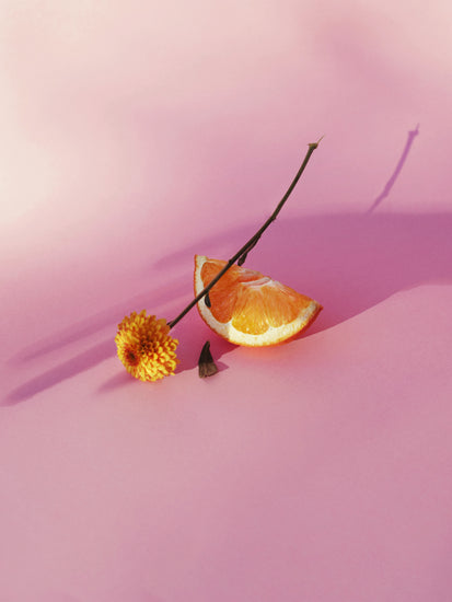 Still life portrait of an orange and a flower on a pink surface.