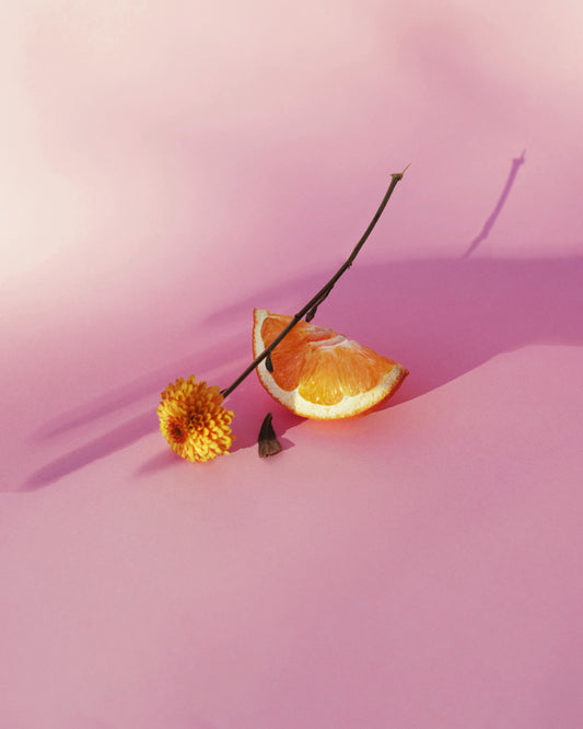 Still life portrait of an orange and a flower on a pink surface.