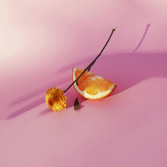 Still life portrait of an orange and a flower on a pink surface.
