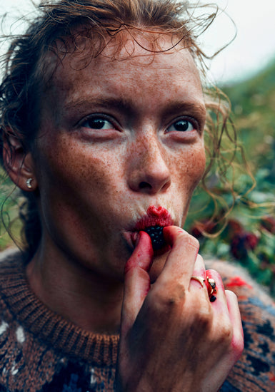 Redheaded woman eating a red berry outdoors.