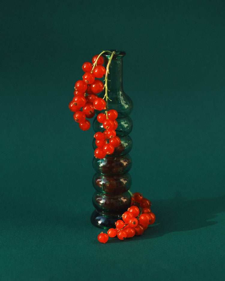 Green glass vase filled with redcurrant berries.