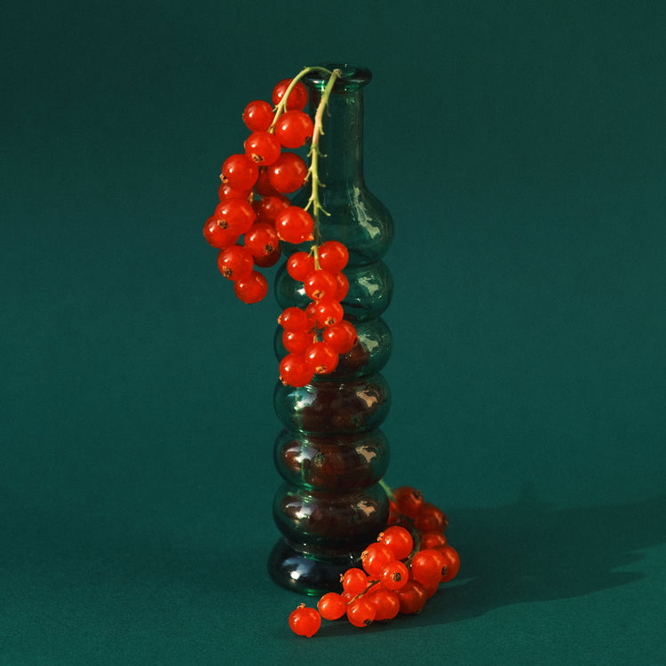 Green glass vase filled with redcurrant berries.