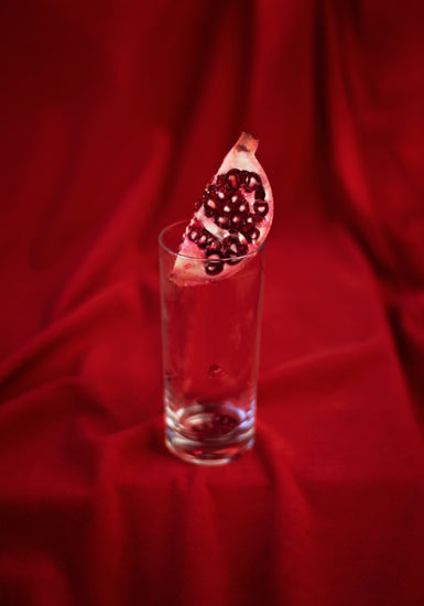 Slice of pomegranate in a glass standing on a blood red sheet.