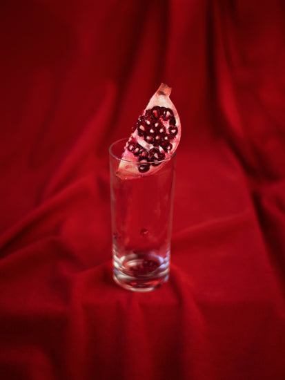 Slice of pomegranate in a glass standing on a blood red sheet.
