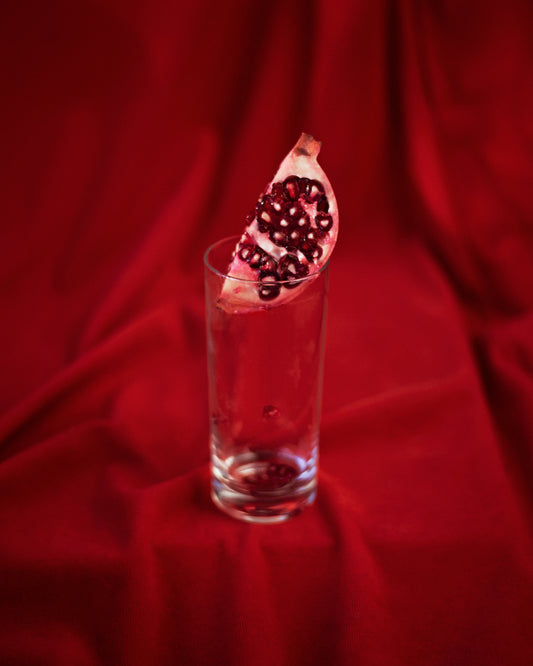 Slice of pomegranate in a glass standing on a blood red sheet.