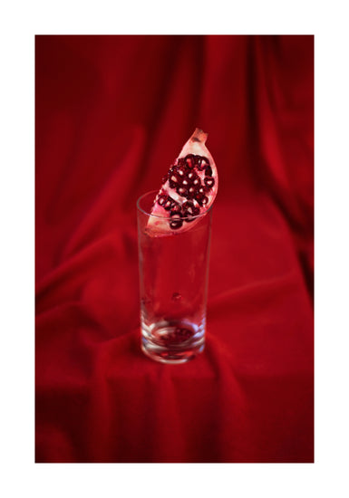 Slice of pomegranate in a glass standing on a blood red sheet.