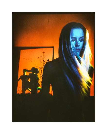 Woman with blonde hair and blue face standing in front of an orange wall.