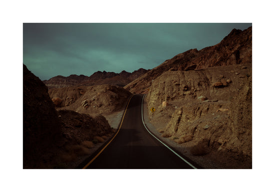 Asphalt road slithering its way through a rough mountain scenery.