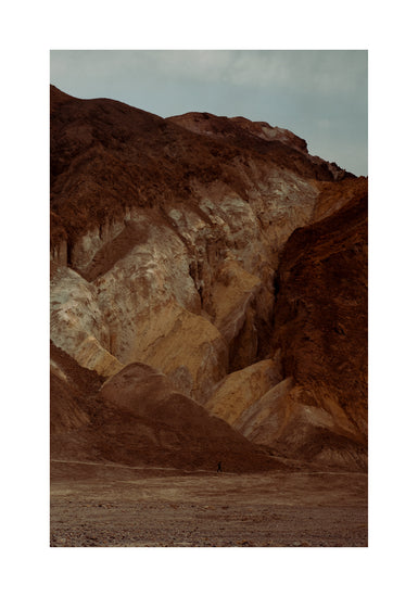 Tiny man walking along the bottom of a massive brown and beige mountain.